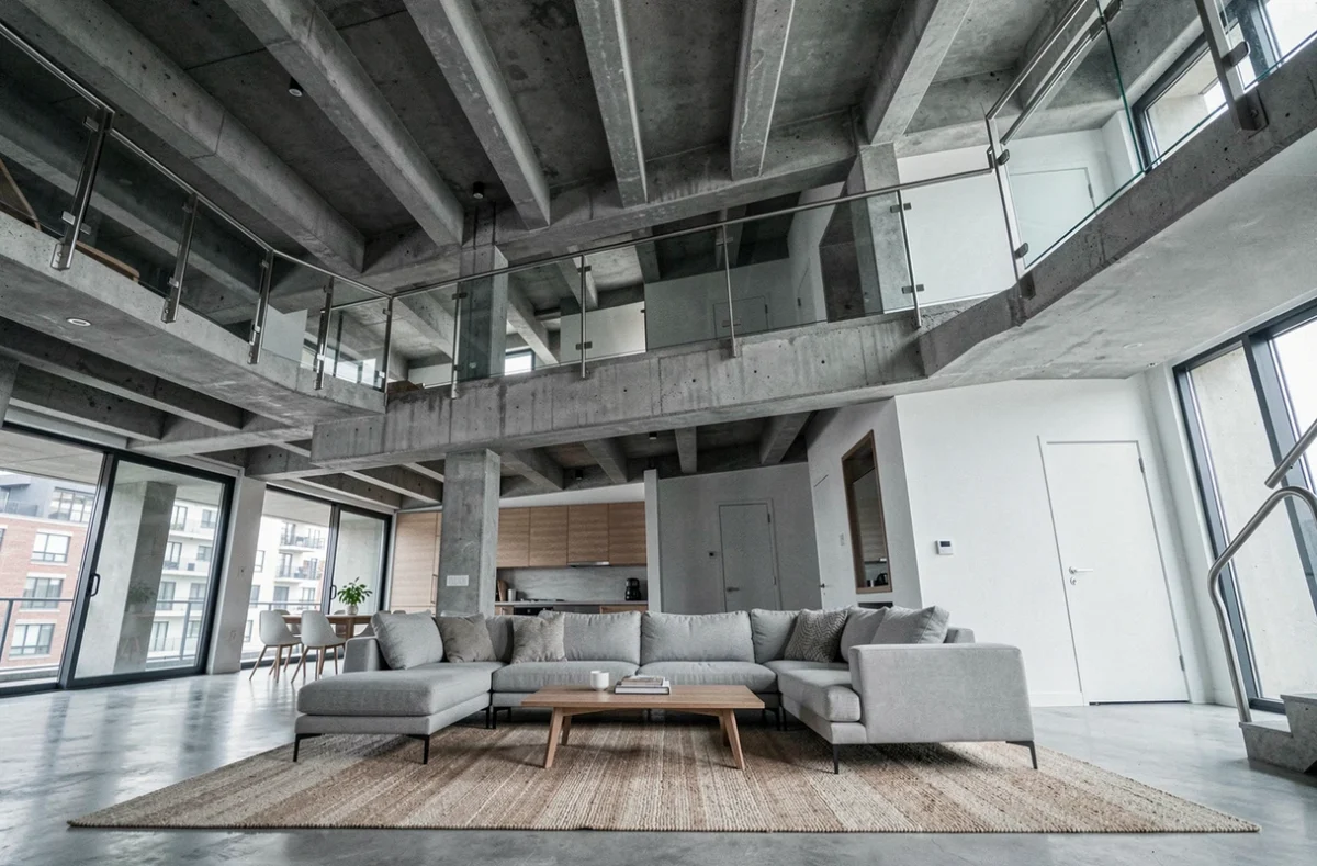 Appartement architecturé avec double hauteur en béton, mezzanine en acier et salon minimaliste