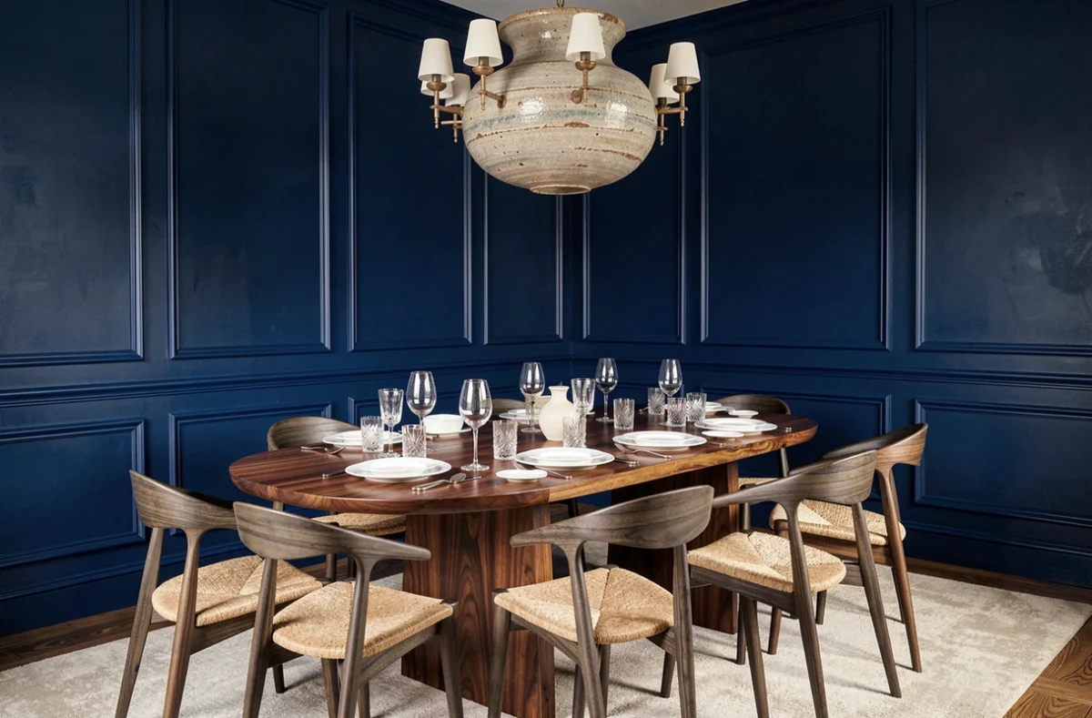 Salle à manger théâtrale mise en scène par Intérieur en Scène avec table ovale en noyer, chaises en frêne fumé et fond laqué bleu nuit